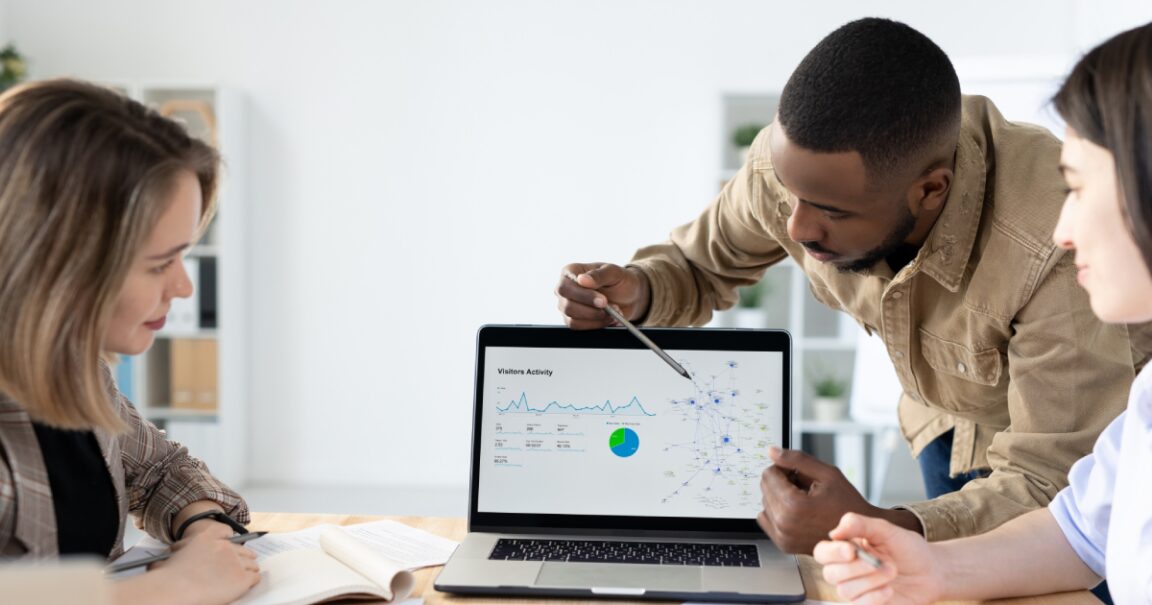 Afro-American marketer pointing at laptop screen while reporting marketing statistics at meeting