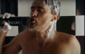 A naked man uses Decore Shampoo as a microphone