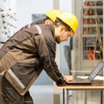 Two maintenance engineers inspect relay protection system with laptop computer. Bay control unit. Medium voltage switchgear
