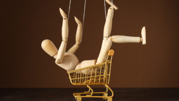 A wooden posable doll sitting in a toy trolley