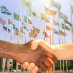 handshake with flags of the world behind it
