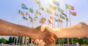 handshake with flags of the world behind it