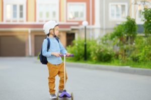 A little boy in safety helmet riding scooter to school