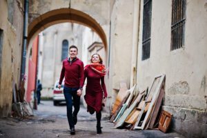 Young beautiful stylish fashion couple in a red dress in love story at the old city, running and having fun together