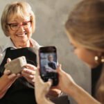 A young women filming a senior woman holding a clay smiling